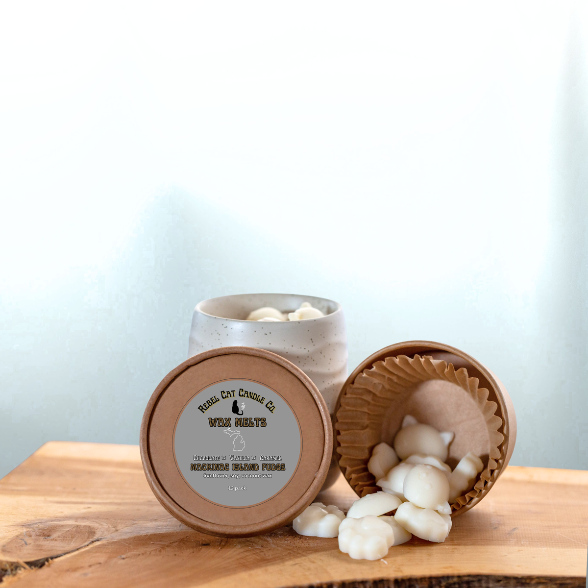 A jar of wax melts with its lid off, showing white wax melts spilling onto a wooden surface next to a ceramic container, on a light blue background.