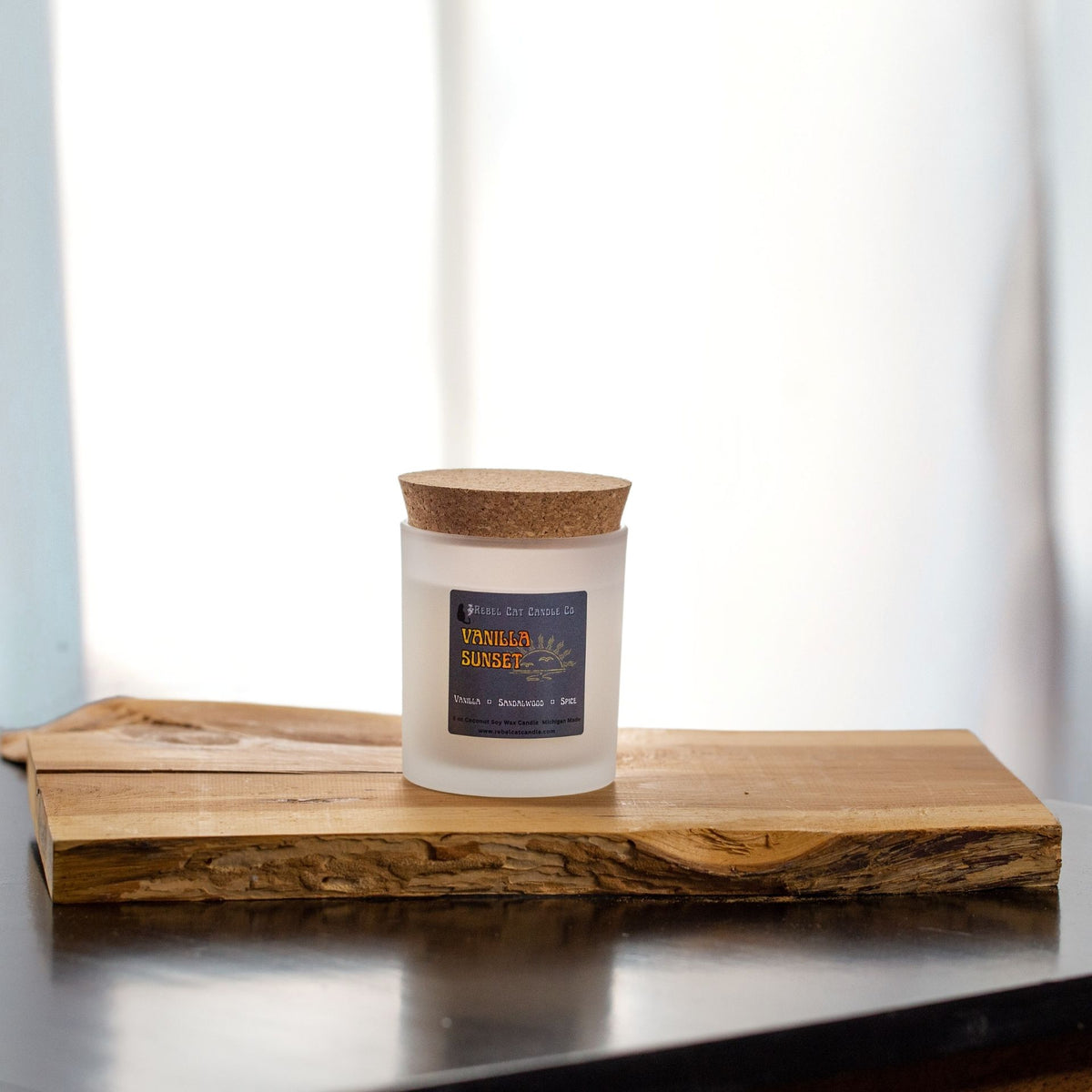 Frosted white 8 oz candle jar with a cork lid sitting on a rustic peice of wood in front of a softly lit window