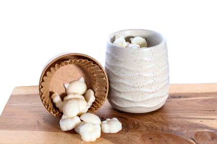 White wax melts displayed on a wooden board, with one ceramic cup tipped over to show the melts spilling out onto the board.