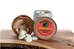 A small round tin of wax melts shown with one lid removed and white wax melts spilled onto a wooden surface next to a ceramic jar of the same product.