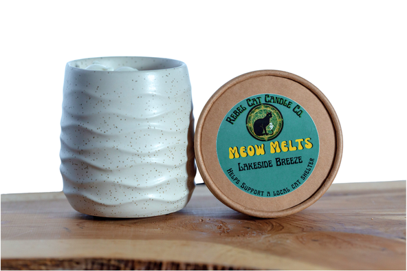 A ceramic  jar with a textured, speckled off-white exterior stands next to a round kraft paper lid. The lid features a teal label with yellow text reading 'MEOW MELTS' and 'LAKESIDE BREEZE' from 'Rebel CAT CANDLE CO.