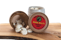 A small round jar of white wax melts with a red lid, shown next to an open container spilling white wax melts on a wooden surface.