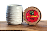 A small white ceramic candle jar with a textured lid and a round red label reading Rebel Cat Candle Co and Meow Melts sits on a wooden surface next to its lid.